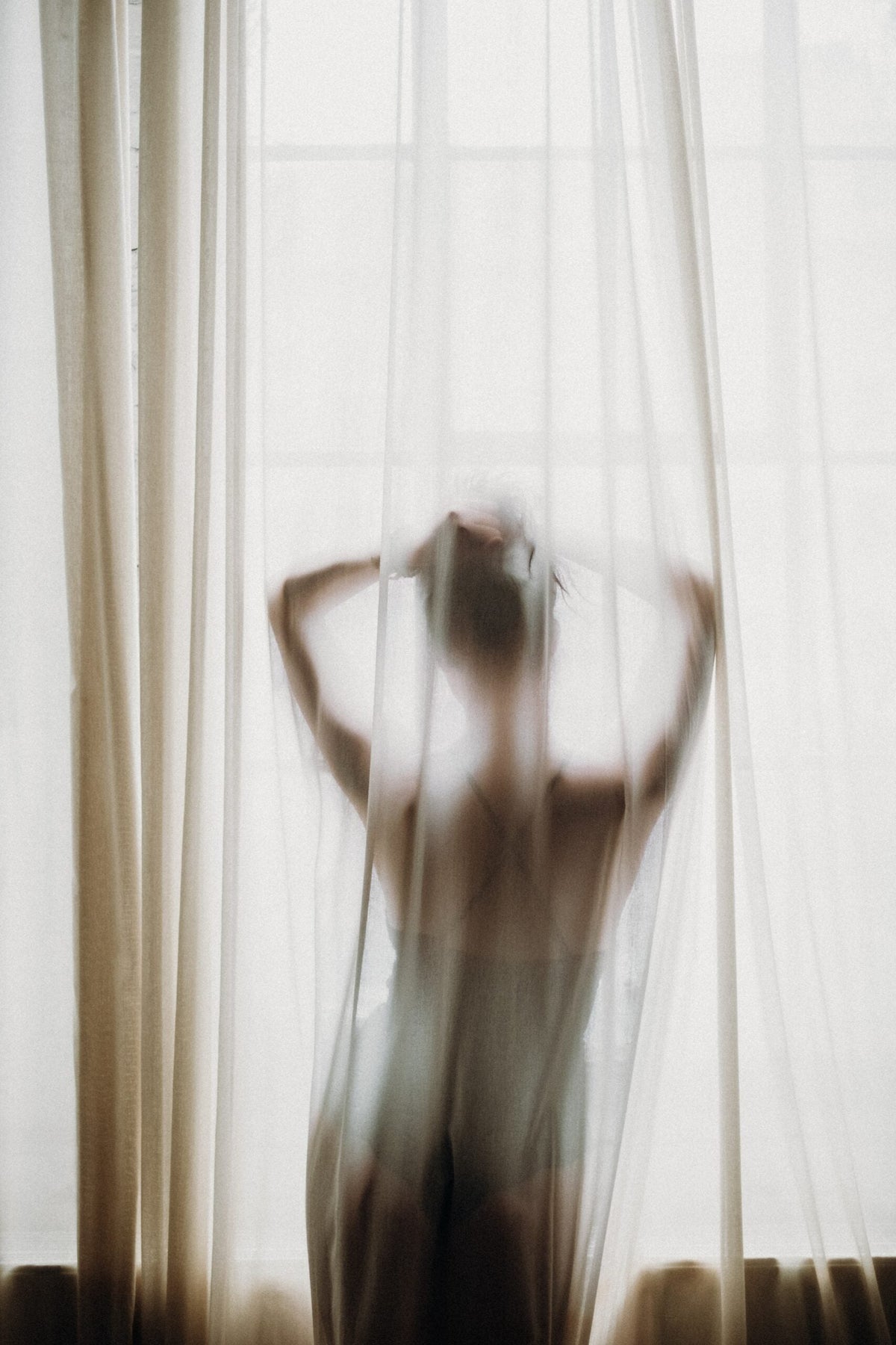 Person standing behind sheer white curtains in soft natural light
