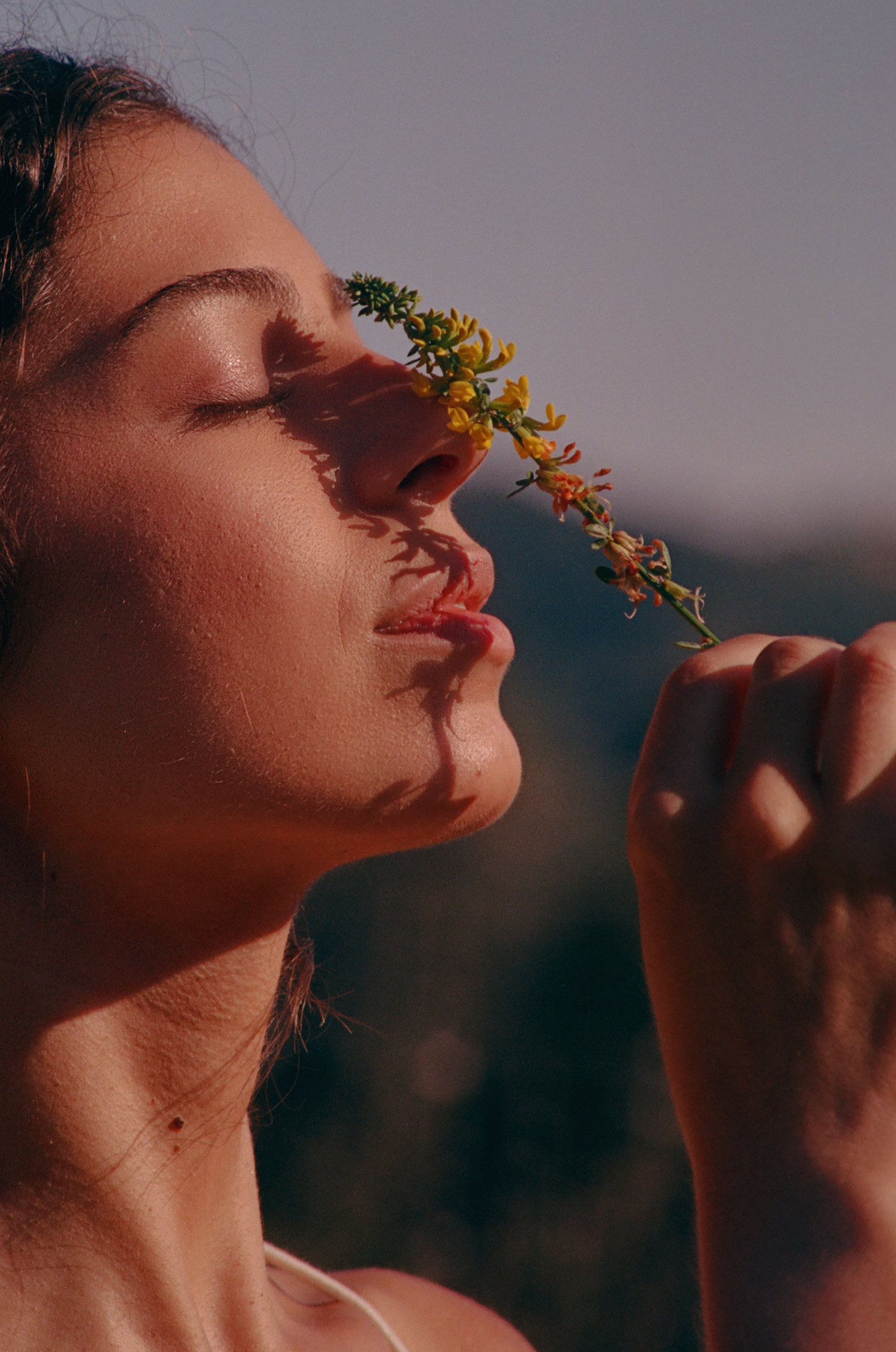 Woman with closed eyes smelling a yellow wildflower held to her nose in warm sunset light
