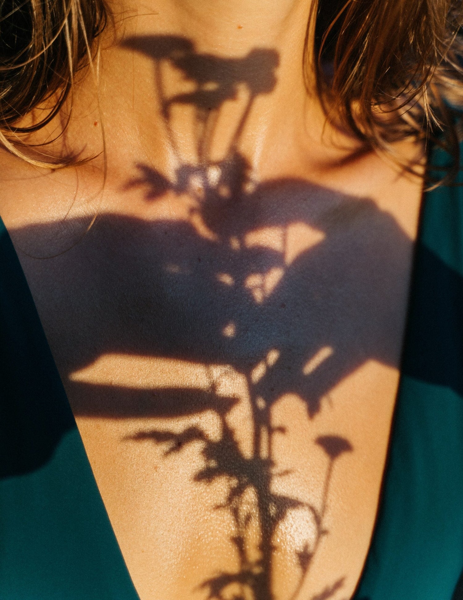 Close-up of a woman’s neck and chest with a plant shadow cast across her skin and a deep green V-neck top