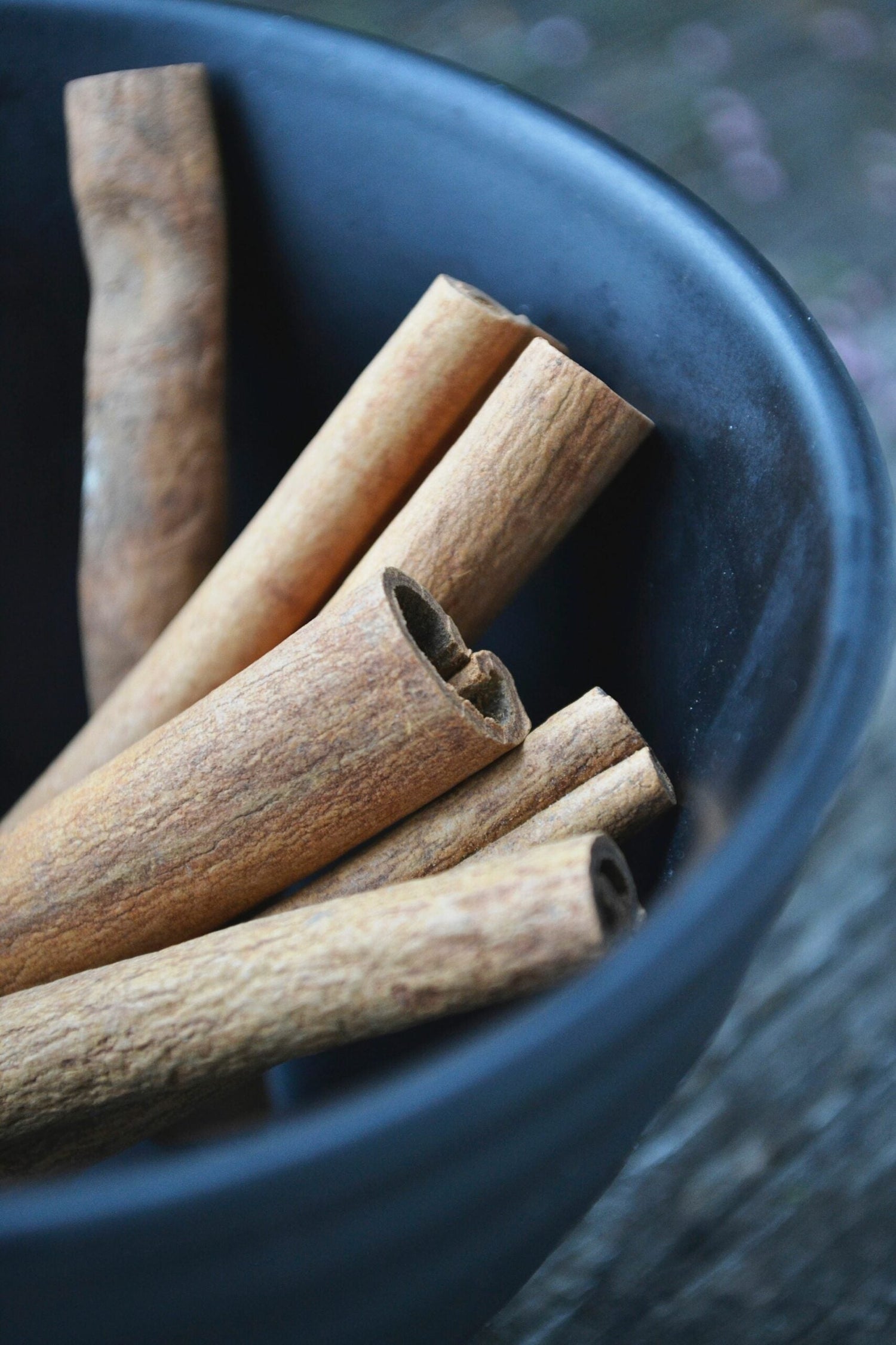 Close up of cinnamon sticks resting in a dark ceramic bowl with a blurred background