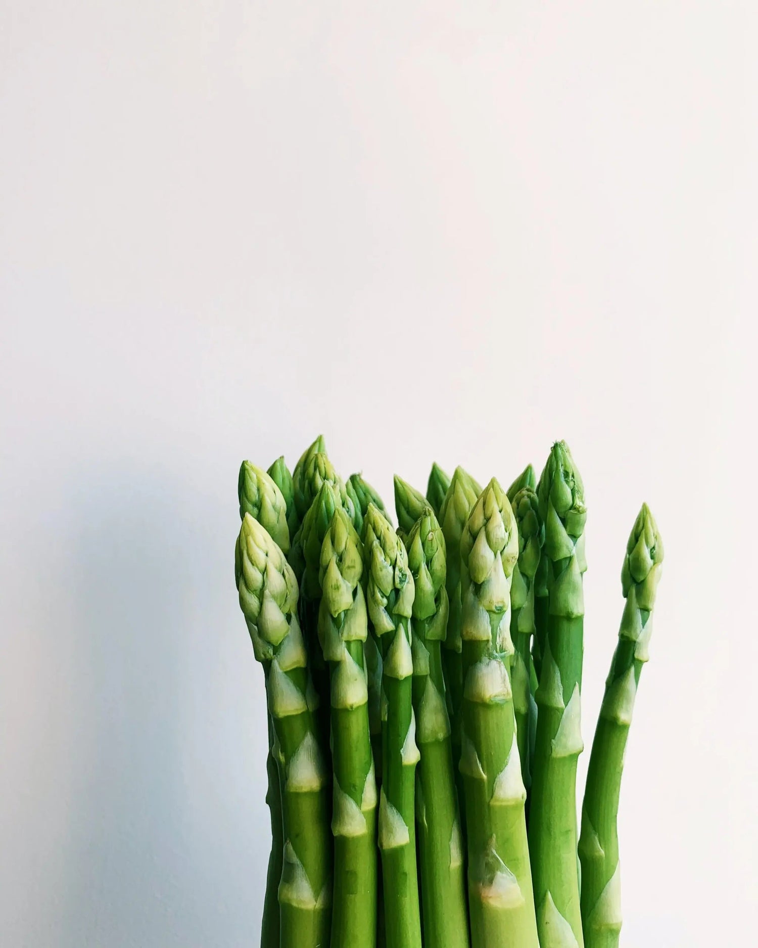 Close up of asparagus spears showing fresh green tips and firm stalks against a pale background