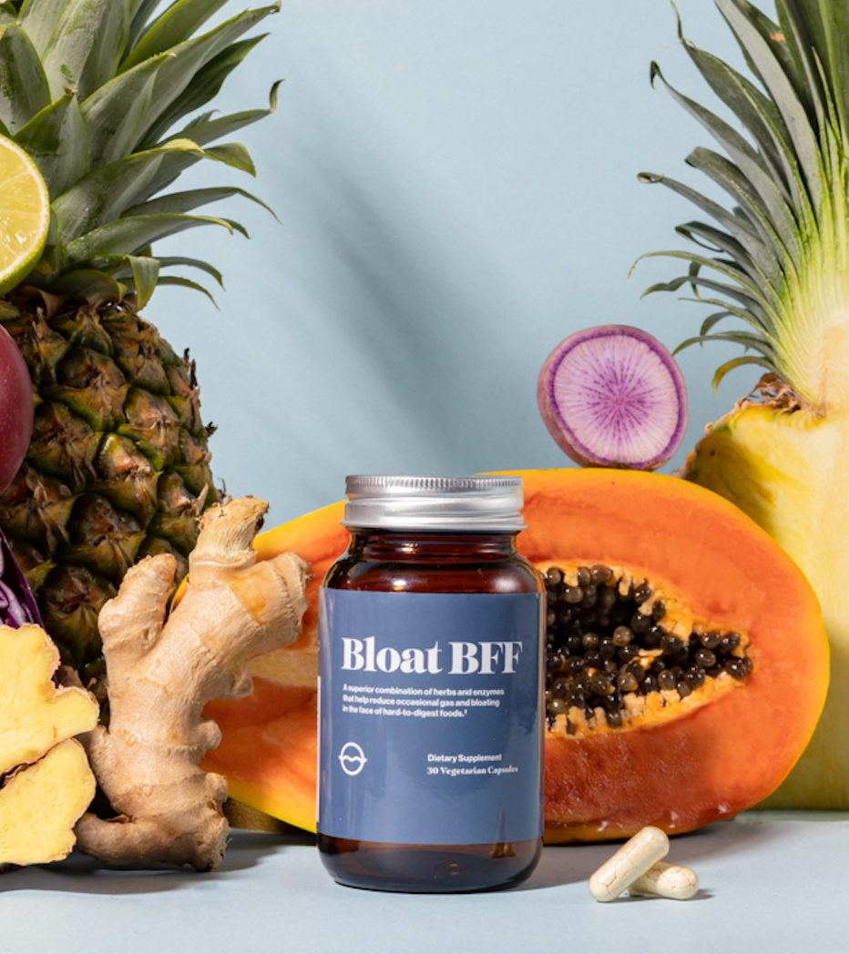 Front view of Bloat BFF dietary supplement bottle with loose capsules, ginger, and colorful fruit on a blue background