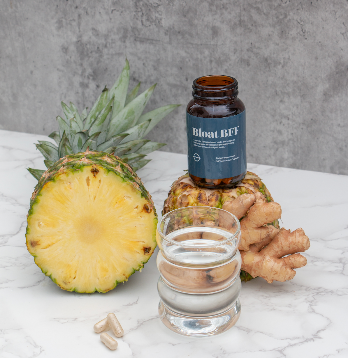 Front view of Bloat BFF supplement bottle showing label and capsules with pineapple and ginger on marble surface