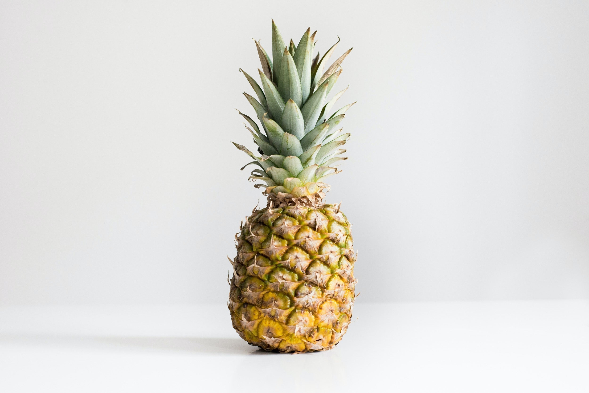 Front view of whole pineapple showcasing textured yellow rind and green spiky crown on a white background