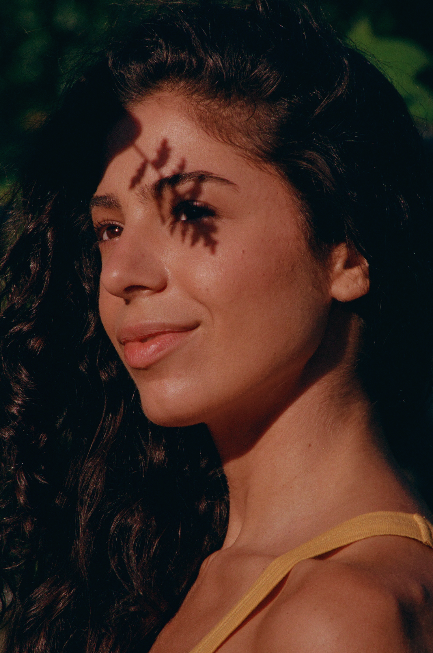 Close-up of a young woman looking right with warm sunlight and a leaf-shaped shadow across her face
