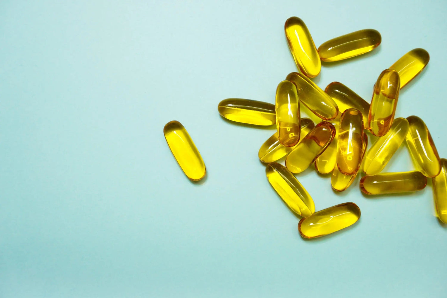 Yellow softgel vitamin capsules scattered on a pale blue background