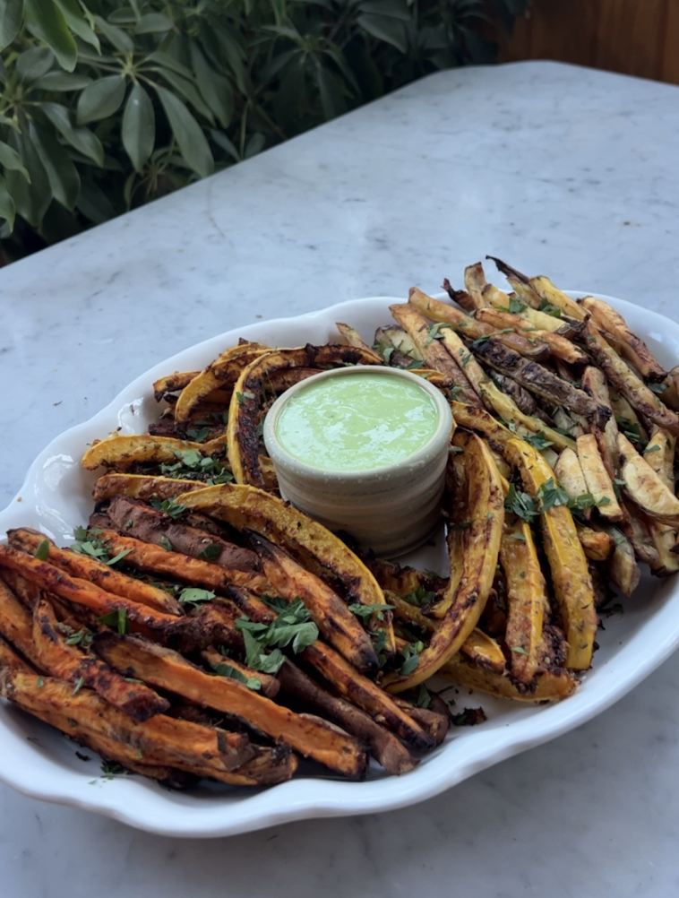 Platter of roasted delicata, sweet potato, and zucchini fries with green herb dipping sauce on marble table