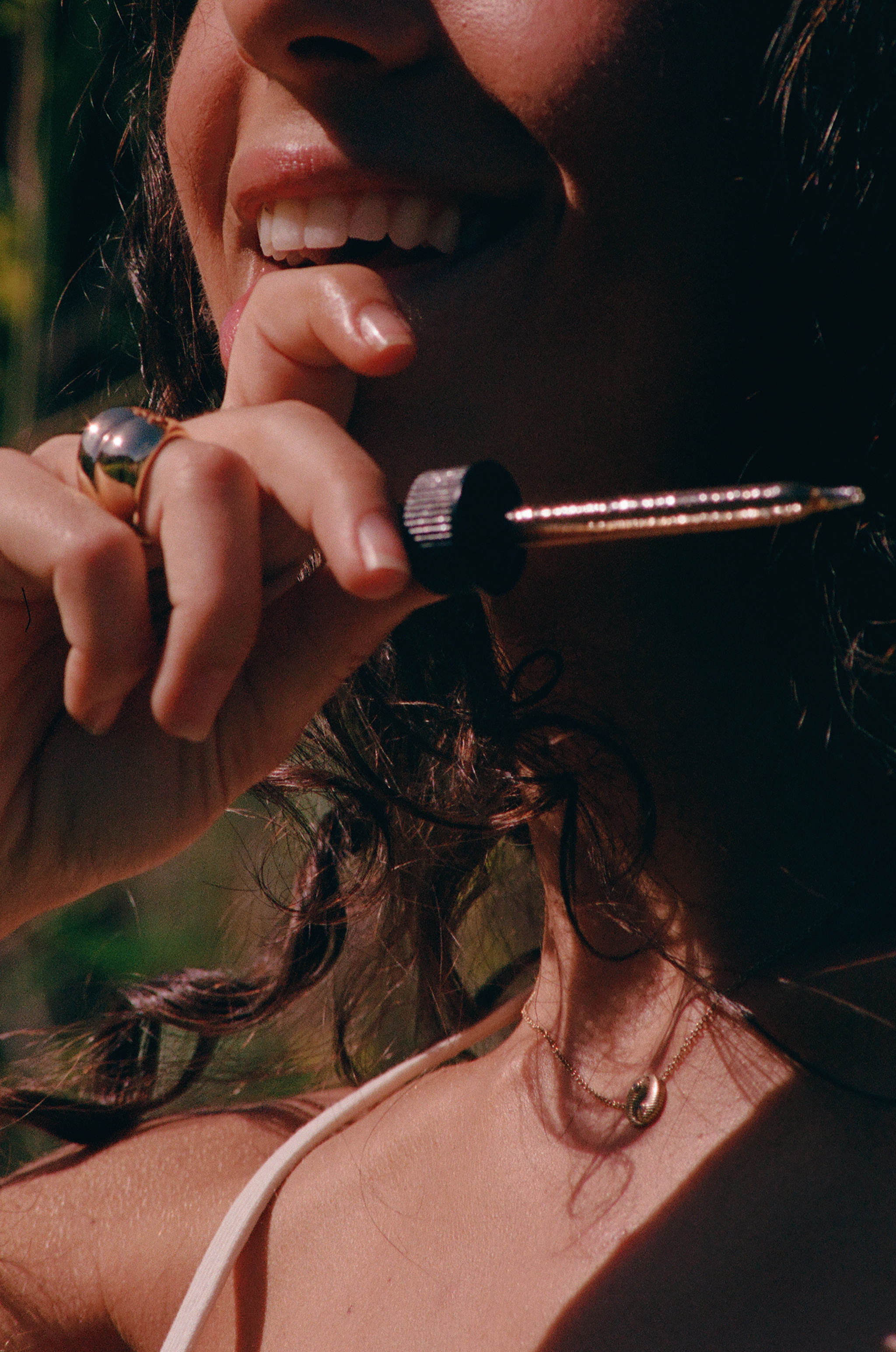 Close-up of a woman smiling while holding a glass dropper near her mouth in sunlight