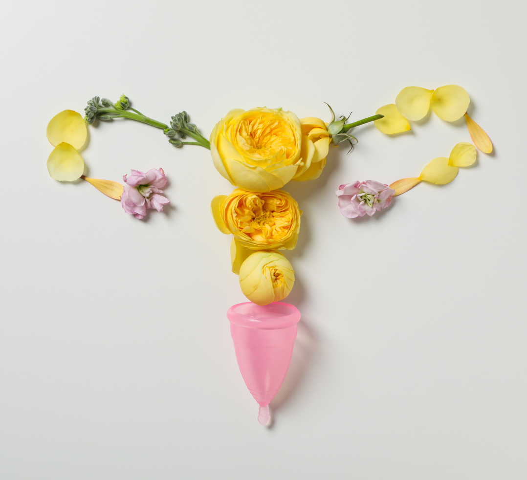 Pink menstrual cup beneath yellow and pink flowers arranged to resemble a uterus on a white background