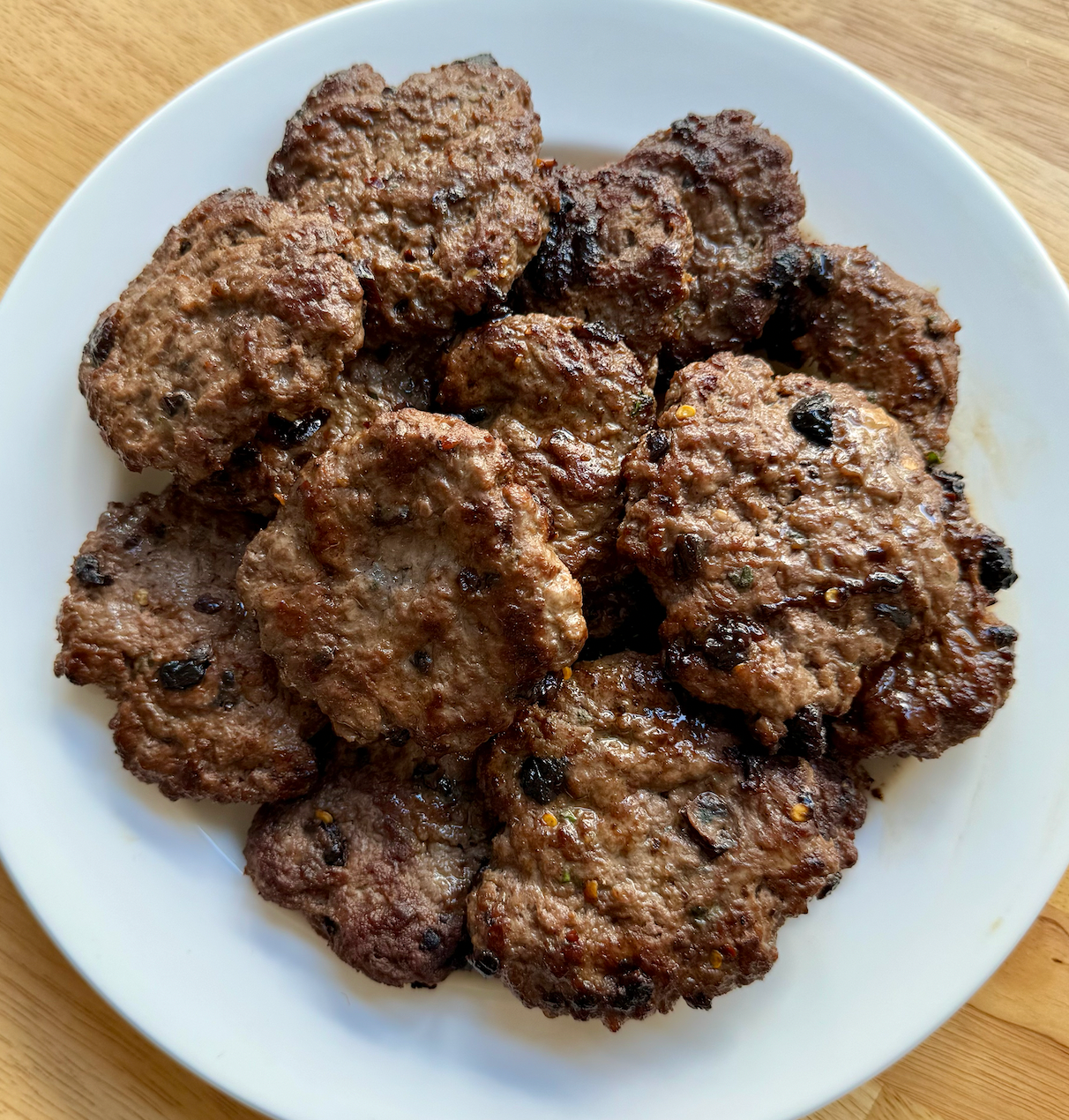 Top-down view of cherry-thyme venison breakfast patties on a white plate, showing browned seared patties with visible cherry pieces and thyme flecks on a wood table
