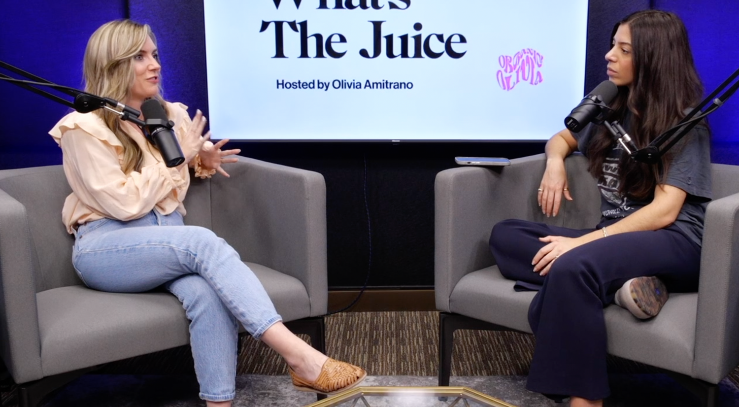 Two women recording a podcast interview in a studio, microphones and a screen behind them displaying “What’s The Juice”