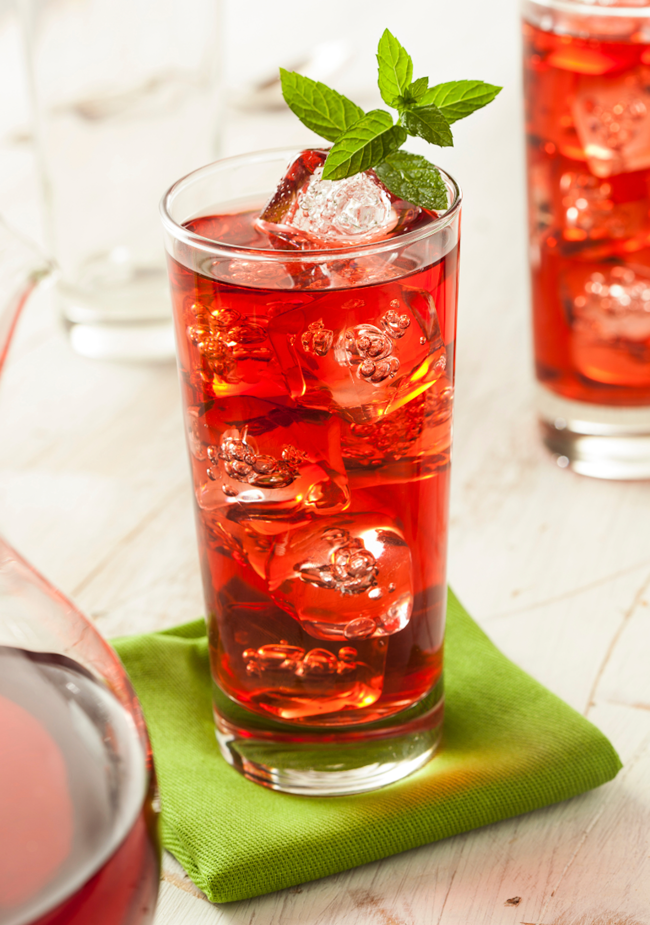Glass of iced red herbal tea garnished with fresh mint on a green napkin