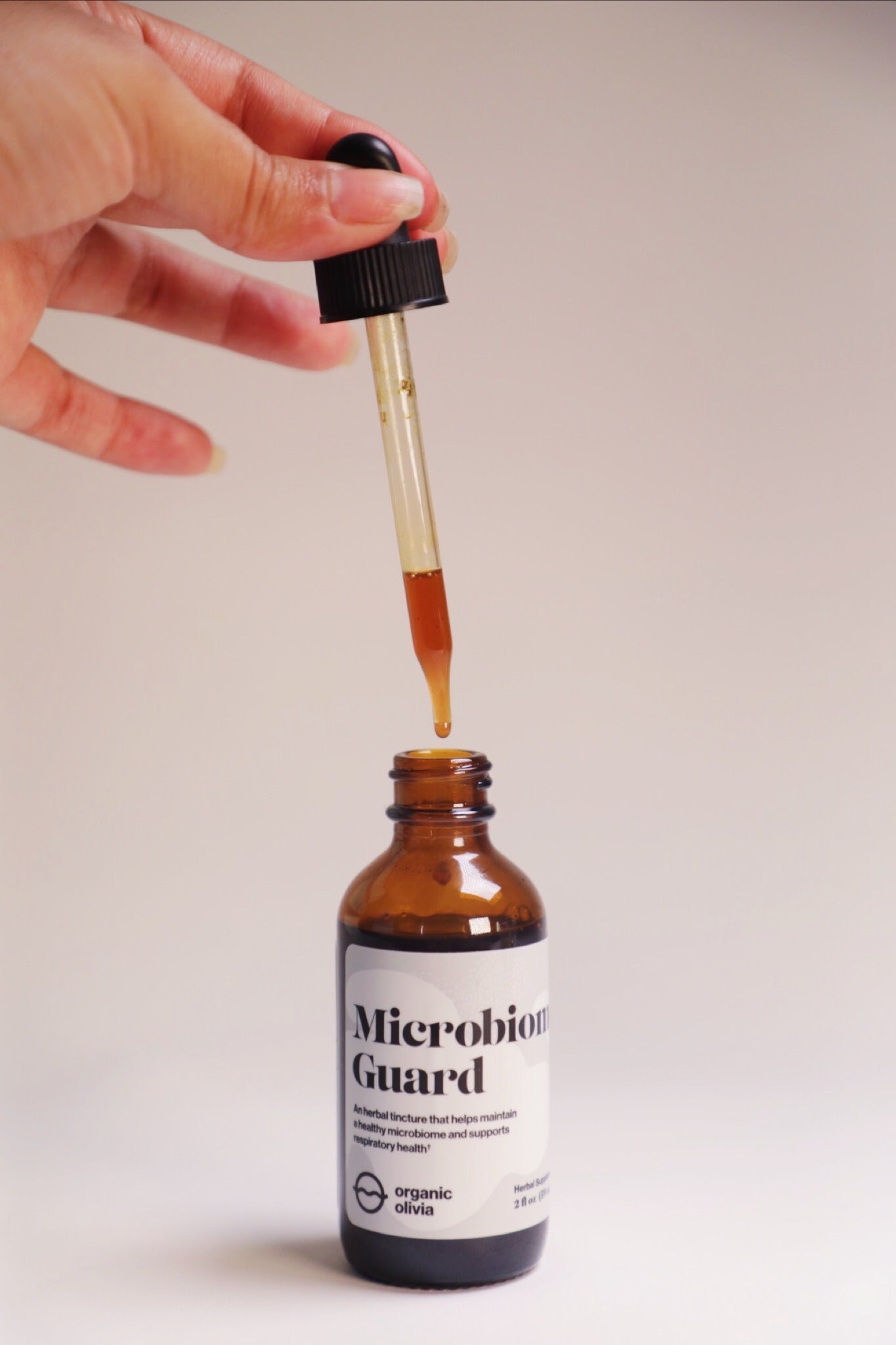 Close-up of an amber Microbiome Guard tincture bottle with a dropper releasing brown liquid against a pale background