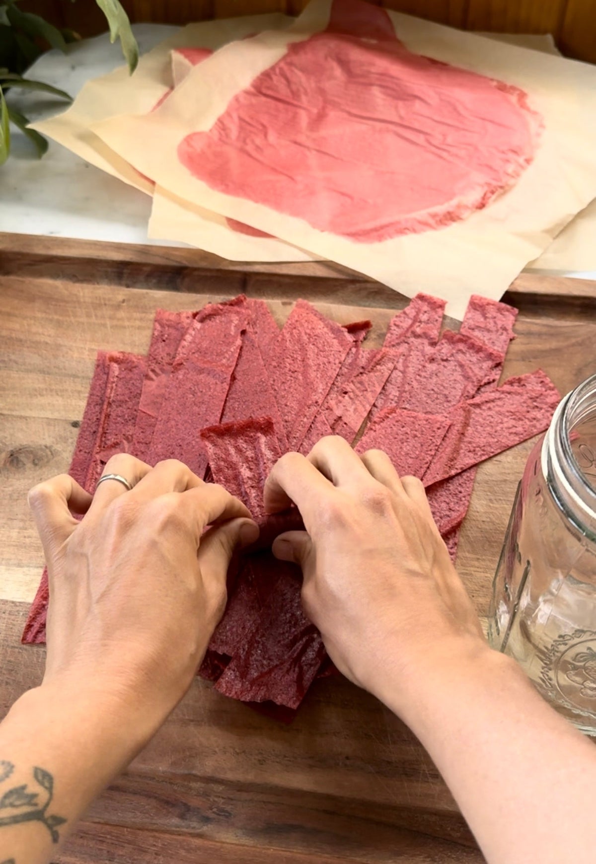 Hands peeling and stacking strips of homemade strawberry rosehip fruit leather on a wooden board