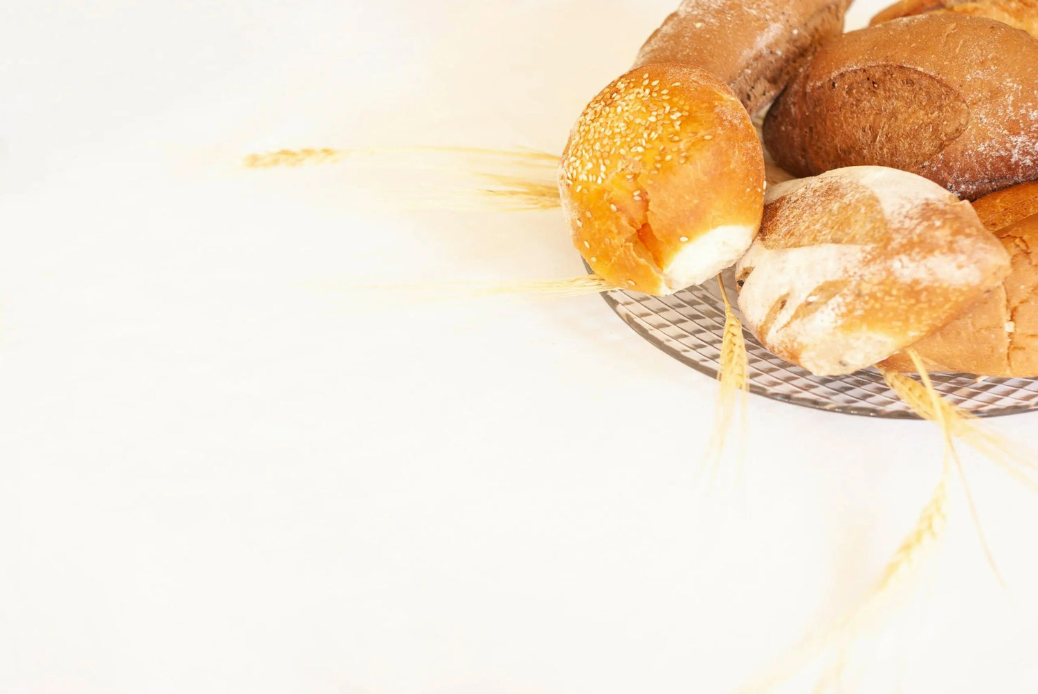 Assortment of bread loaves with wheat stalks on a round plate against a pale background