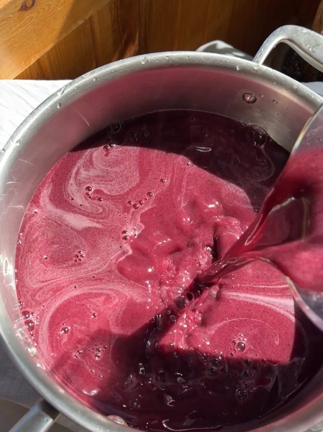 Blueberry mixture being poured into a stainless steel pot while making herbal gummies, lit by warm natural light
