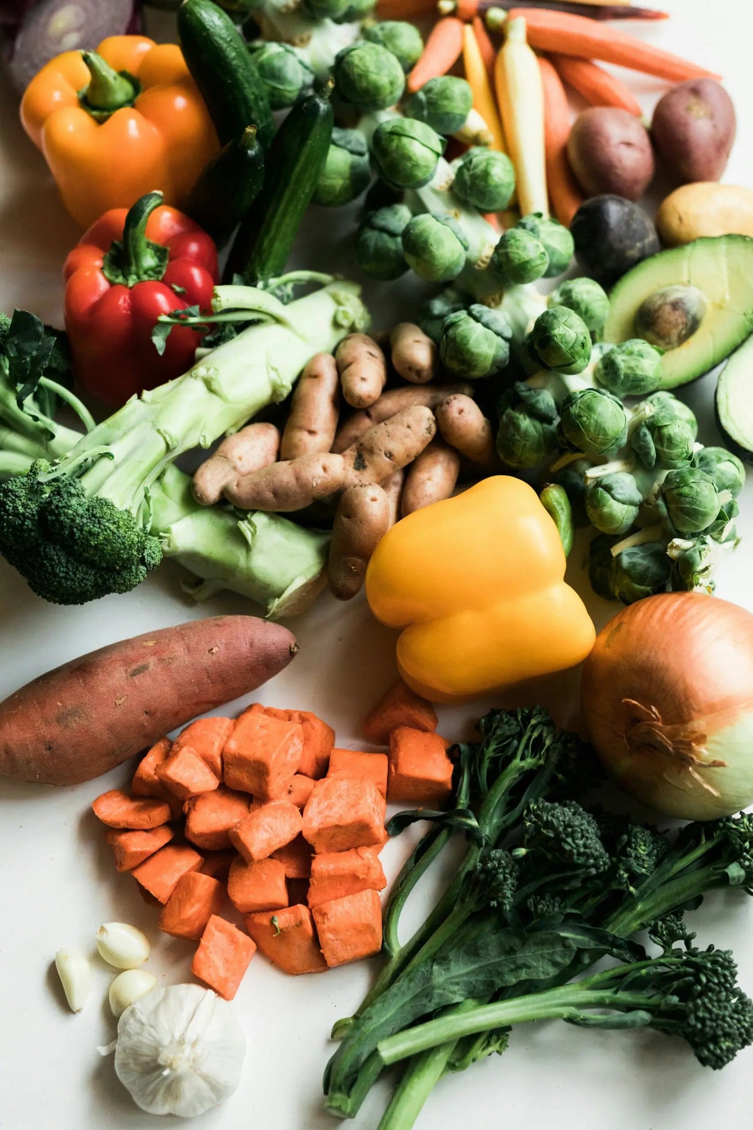 High-fiber vegetables on a white surface: diced sweet potato, broccoli, Brussels sprouts, bell peppers, avocado, garlic