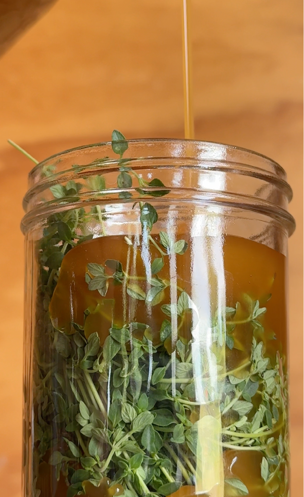 Fresh thyme in a jar as honey is poured in to make an oxymel