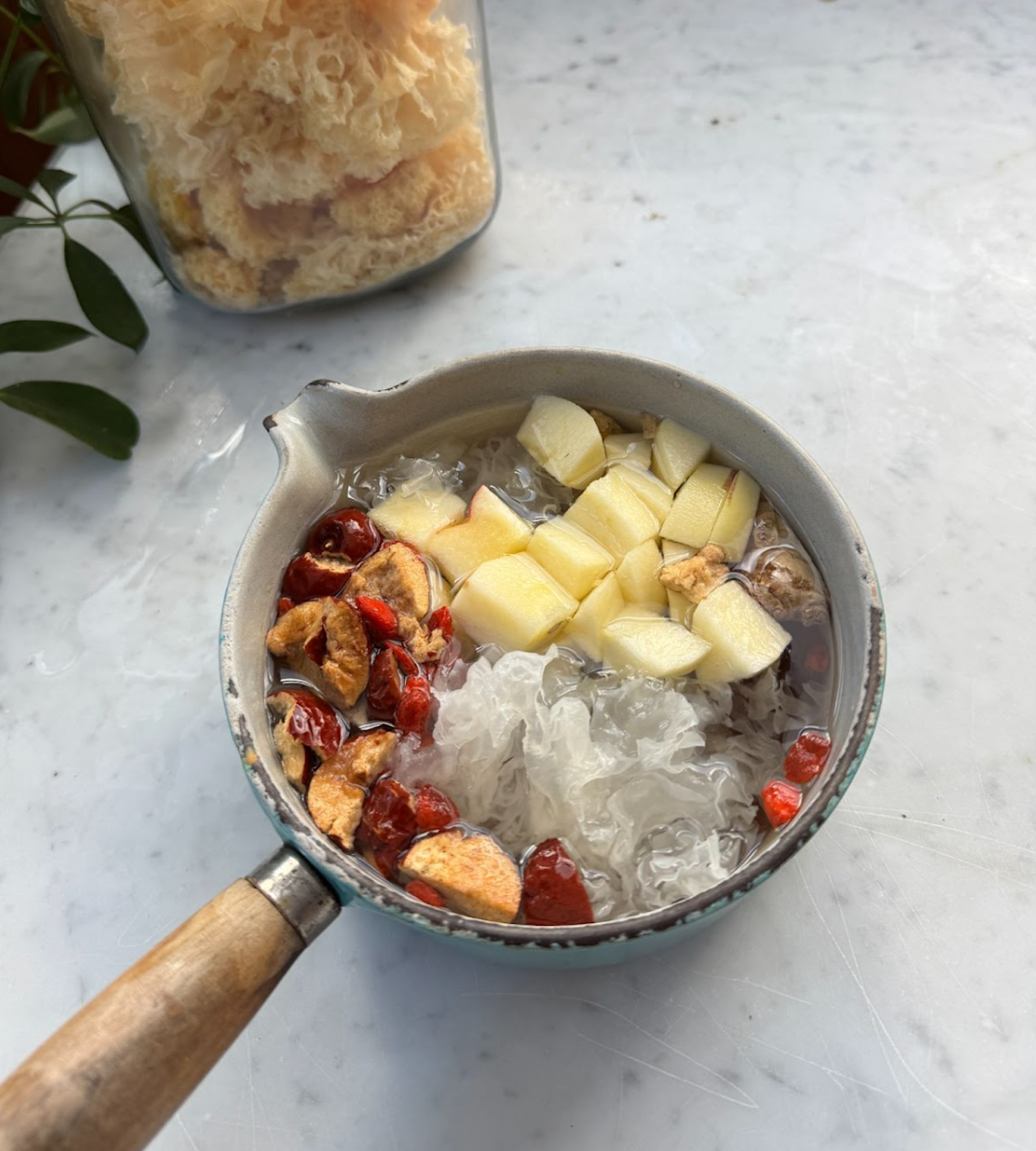 Small saucepan of tremella mushroom dessert soup served with diced apple, dried jujube, and goji berries on a marble countertop