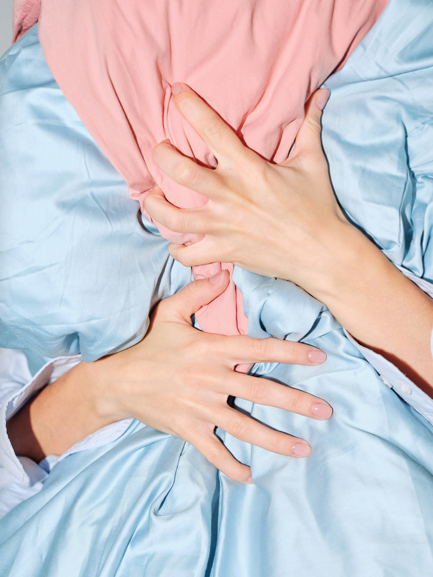 Hands clutching a pink pillow and blue sheets suggesting nighttime chest discomfort in bed