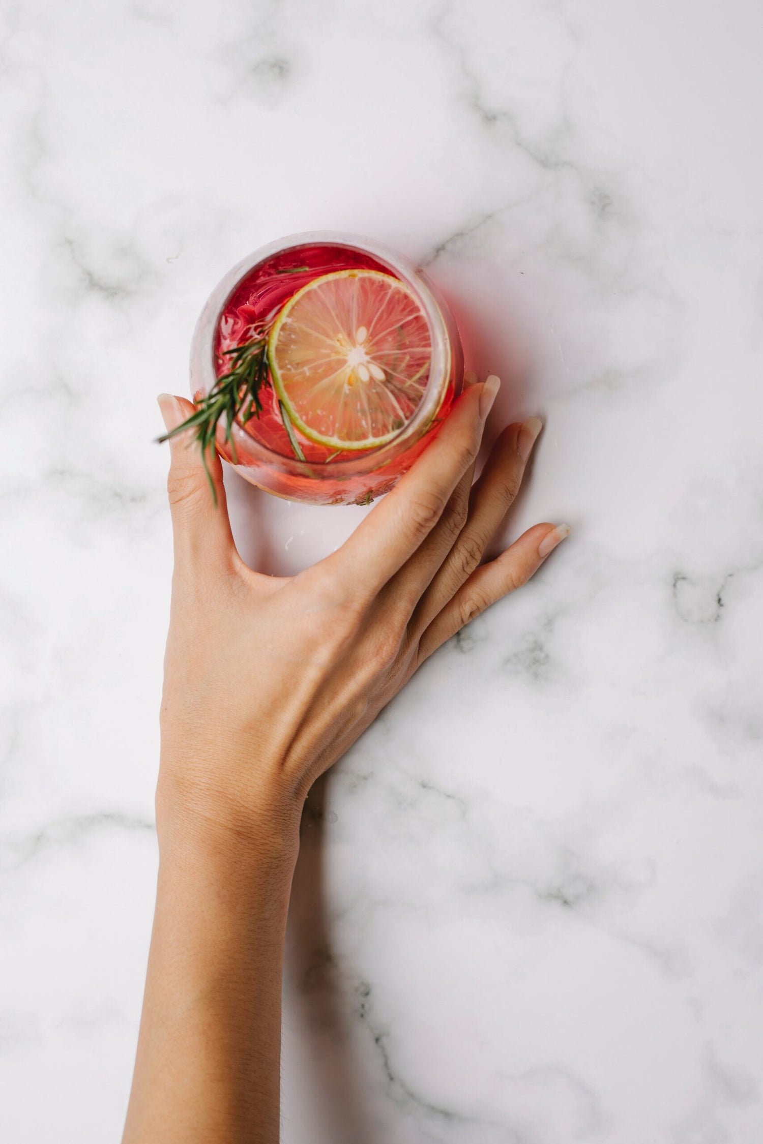 hand holding a pink cocktail with rosemary and a citrus slice